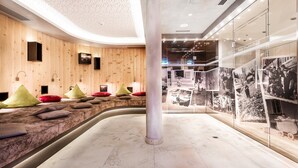 Un moderno espacio de spa con paneles de madera, un banco curvo con cojines y una vitrina con fotografías históricas.