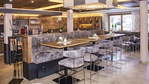 Un restaurante moderno con mesas altas, taburetes de bar, una zona de bar y un área de asientos con bancos acolchados.