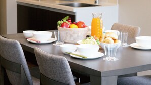 Une cuisine moderne avec une table à manger mise pour le petit-déjeuner, comprenant des bols, des assiettes, des verres et un panier de fruits.