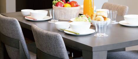 A modern kitchen with a dining table set for breakfast, including bowls, plates, glasses, and a fruit bowl.