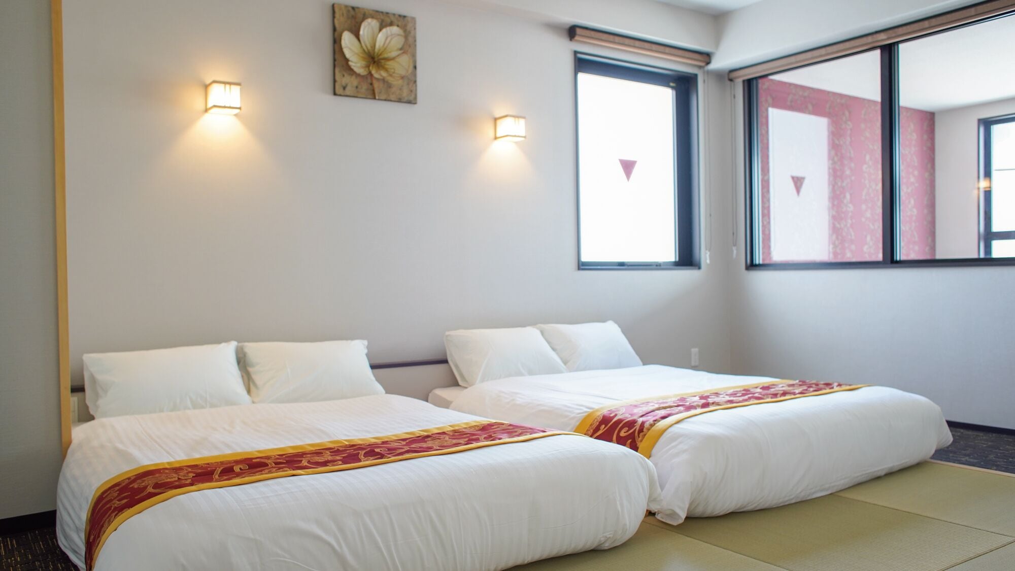 A hotel room with two beds, a large window, and wall-mounted lights.