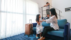 Une pièce avec un canapé bleu, un enfant assis par terre, un autre enfant sur une échelle et une valise.