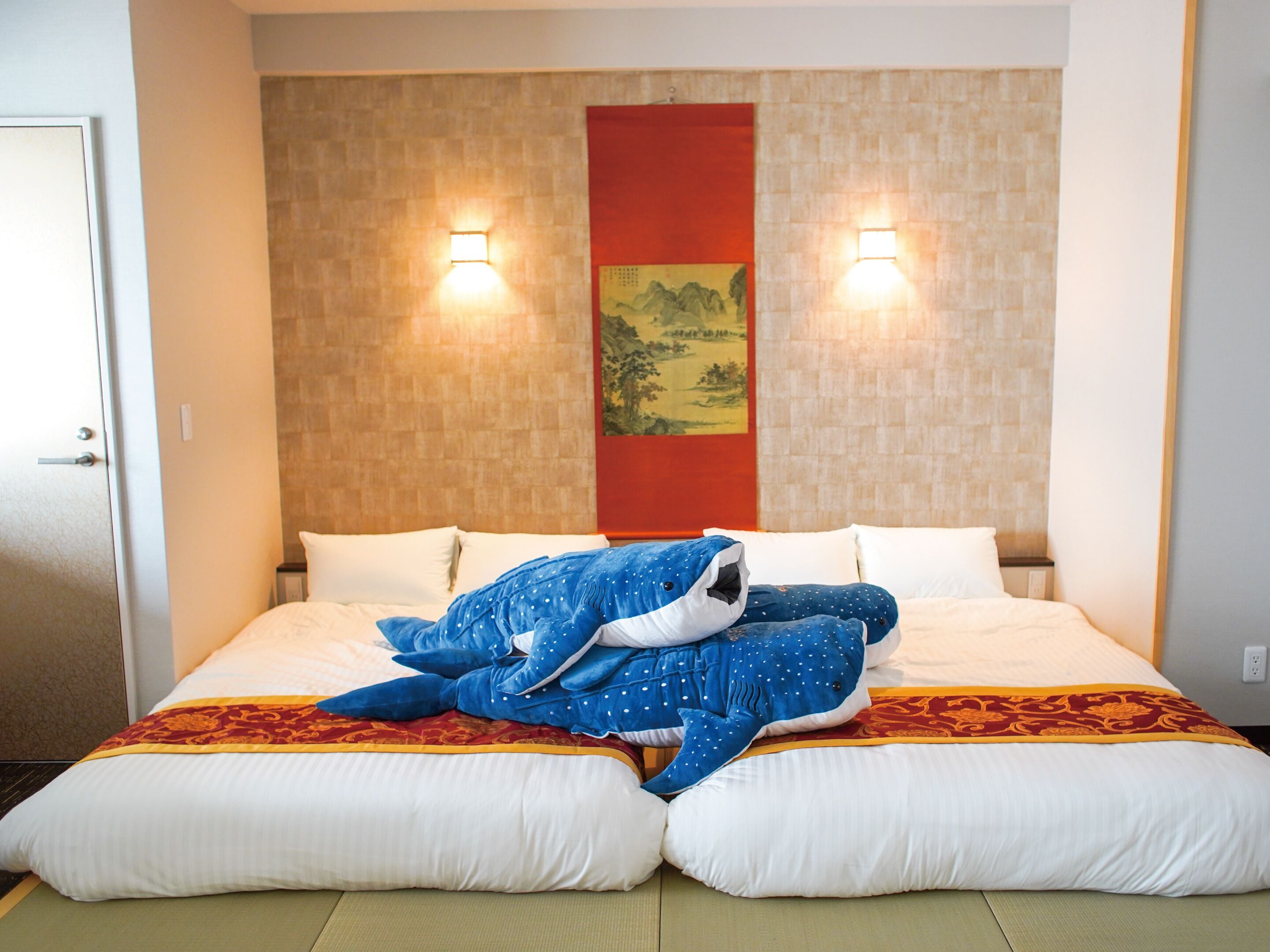 A hotel room with a bed, pillows, a blanket, and a wall-mounted light fixture.