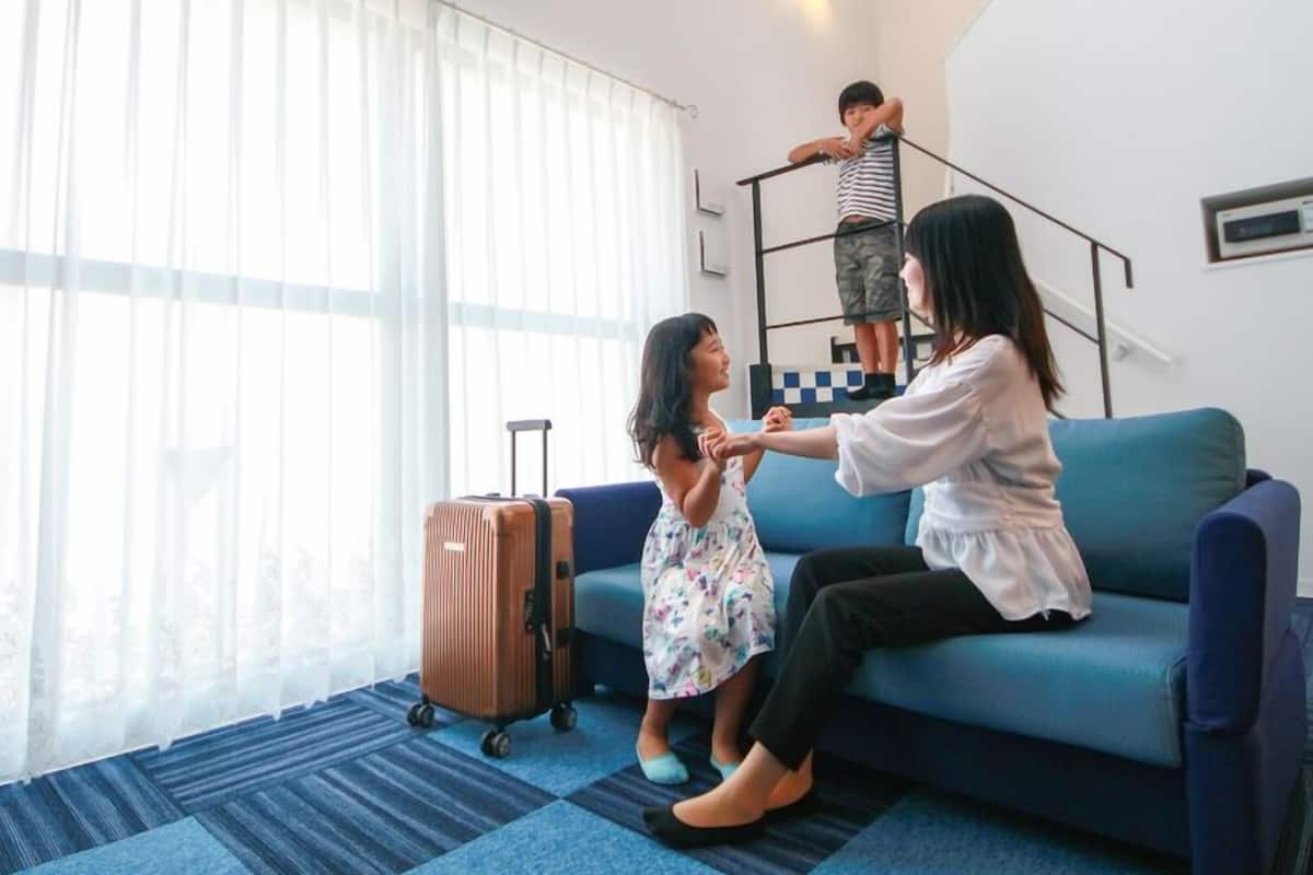 Een kamer met een blauwe bank, een kind met een koffer en een persoon op een klein platform.