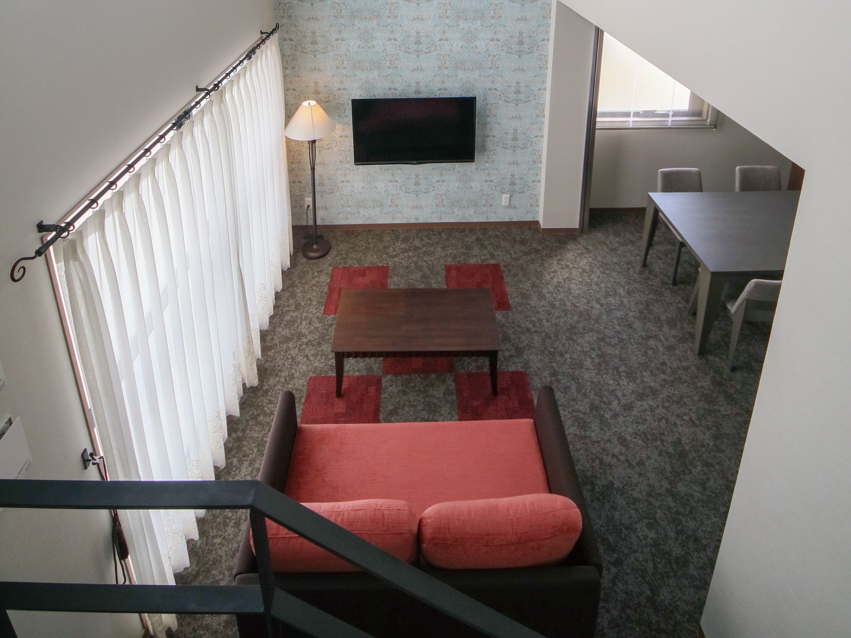 A room with a staircase, a sofa, a table, and a TV mounted on the wall.