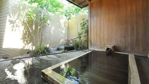 Een traditionele Japanse onsen met een houten interieur, een stenen bad en een klein houten bankje.