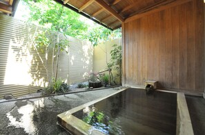 A traditional Japanese onsen with a wooden interior, a stone bath, and a small wooden bench. - Higashi Ishikawa Ryokan (Matsumoto)
