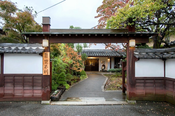 A traditional Japanese gate with a pathway leading to a building with a tiled roof.