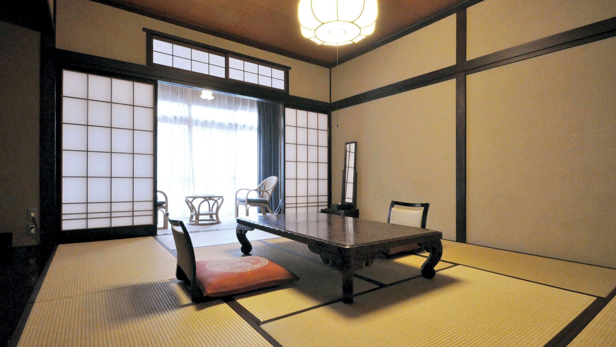 A tatami mat room with a low table, chairs, and a sliding door.