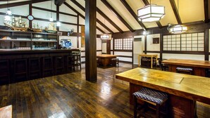Een traditionele Japanse bar met houten vloeren en zichtbare balken, met een toonbank met diverse artikelen en een klok aan de muur.