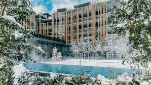 Un bâtiment moderne à la façade vitrée, entouré d’arbres couverts de neige et agrémenté d’une piscine.