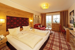 A hotel room with a large bed, a desk, a red sofa, and a view of the outdoors. - DOUBLE ROOM CLASSIC - 5* Wellness & Sporthotel Jagdhof (Röhrnbach)