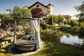 Ein Garten mit einer Sitzgruppe in Kreisform, einem Teich und einem Gebäude im Hintergrund.