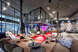 A spacious lobby with modern seating, a large window, and a staircase leading to an upper level. - DREAM SUITE - 5* Wellness & Sporthotel Jagdhof (Röhrnbach)