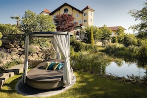 A garden with a circular seating area, a pond, and a building in the background. - DREAM SUITE - 5* Wellness & Sporthotel Jagdhof (Röhrnbach)