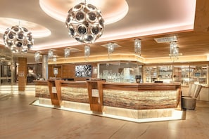 A modern hotel lobby with a reception desk, wooden accents, and decorative lighting fixtures.