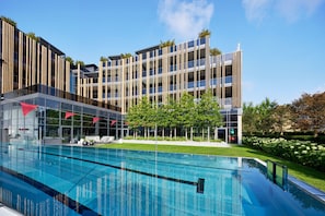 A modern hotel with a swimming pool, multiple balconies, and a well-maintained garden. - ROMANTIK-SUITE - 5* Wellness- & Sporthotel Jagdhof (Röhrnbach)