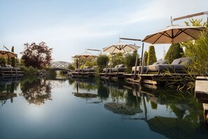 A tranquil outdoor pool area with lounge chairs and umbrellas, surrounded by greenery and a clear sky. - DOUBLE ROOM BERGKRISTALL - 5* Wellness & Sporthotel Jagdhof (Röhrnbach)