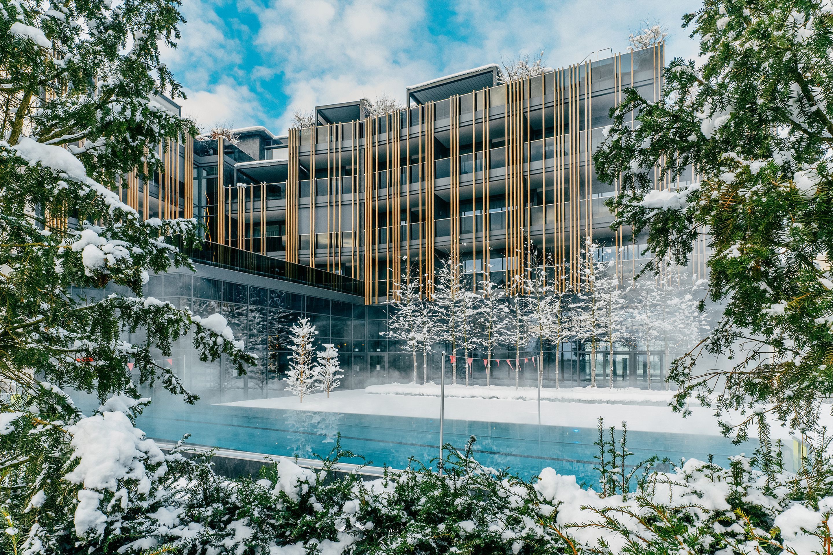 Ein modernes Gebäude mit Glasfassade, umgeben von schneebedeckten Bäumen und einem Pool.