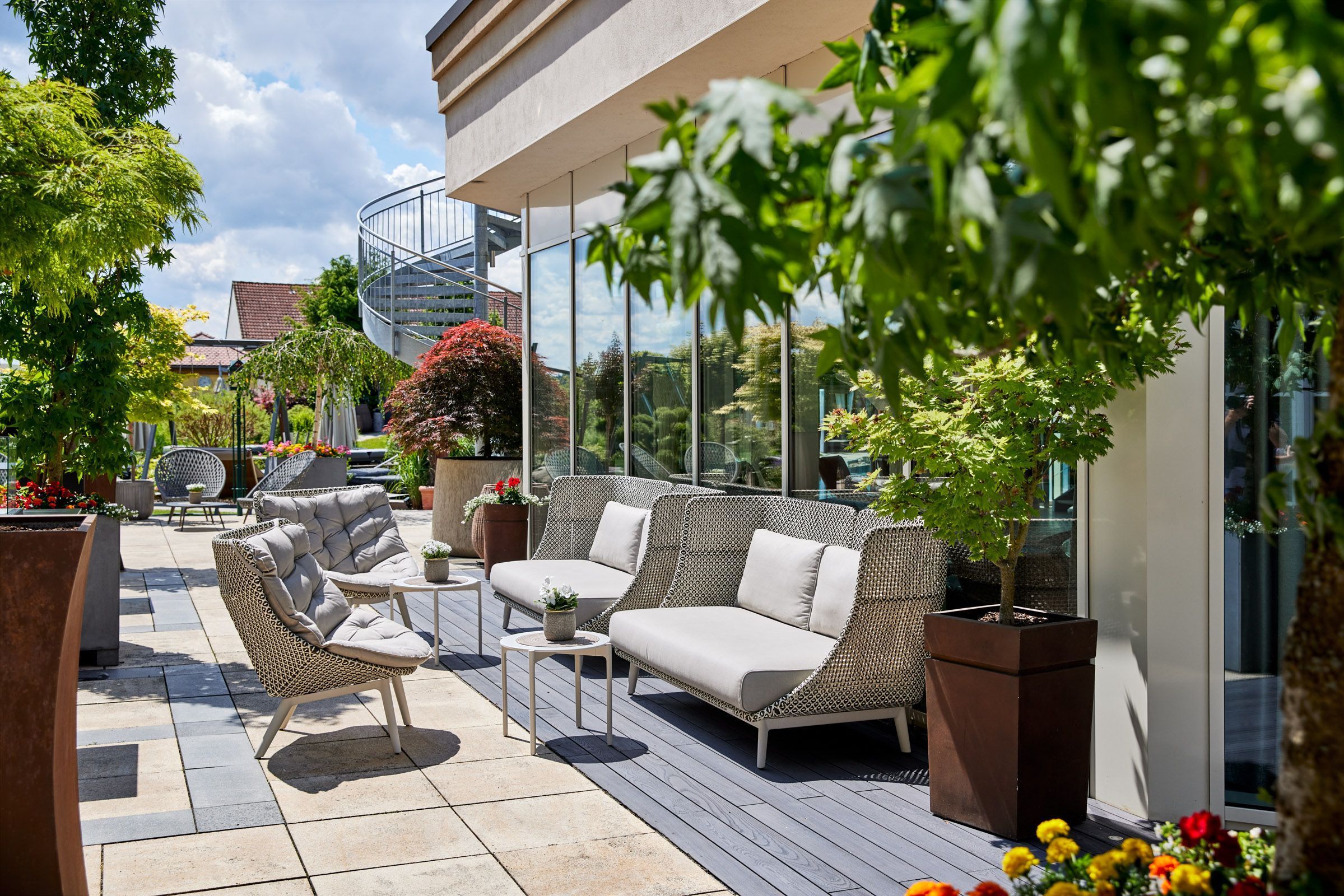 A patio with wicker furniture, a glass balustrade, and potted plants.