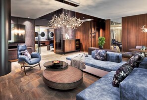 A modern living area with a sofa, armchair, coffee table, and a chandelier. - JAGDHOF-SUITE - 5* Wellness- & Sporthotel Jagdhof (Röhrnbach)