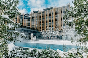 Un bâtiment moderne à la façade vitrée, entouré d’arbres couverts de neige et agrémenté d’une piscine.
