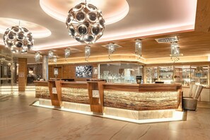 Un hall d’hôtel moderne avec un comptoir d’accueil, des éléments décoratifs en bois et des luminaires décoratifs.
