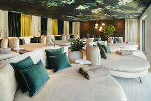 A modern hotel room with a curved sofa, a small round table, and a large potted plant.