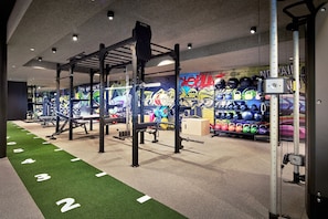 Une salle de sport équipée de matériel de musculation, dotée d’une piste d’athlétisme en gazon synthétique et d’un mur orné de graffitis colorés.