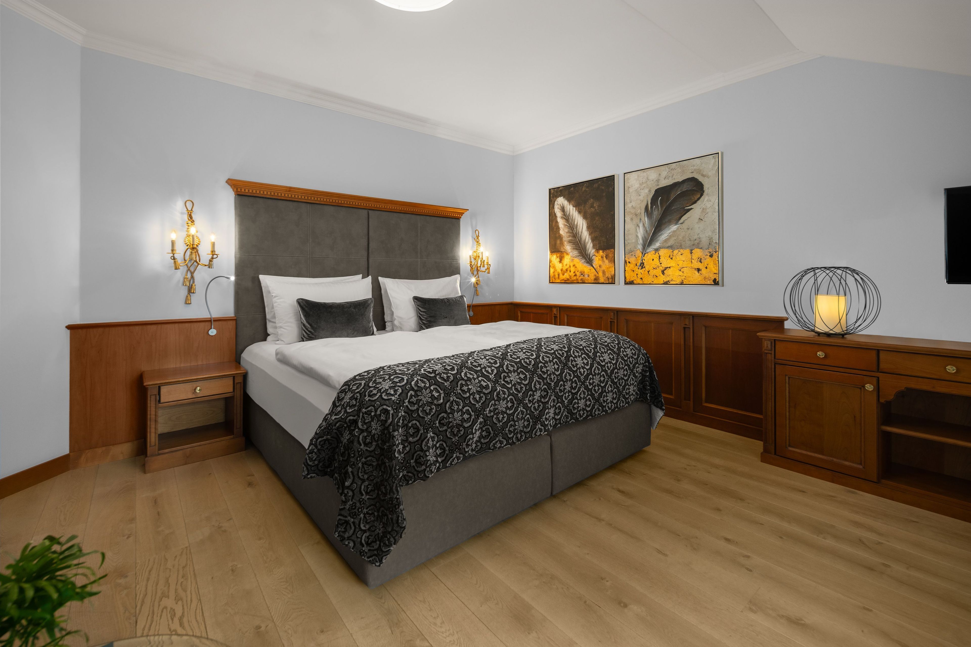 A bedroom with a large bed, wooden nightstands, a dresser, and wall-mounted artwork.