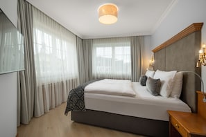 A modern hotel room with a large bed, a flat-screen TV, a bedside table, and a ceiling light fixture.