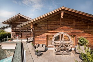 Una cabaña de madera con piscina, mobiliario exterior y una gran rueda de madera.