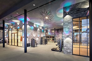 A gym with exercise equipment, a brick wall, and a large window. - SCHLÖSSL-SUITE - 5* Wellness- & Sporthotel Jagdhof (Röhrnbach)