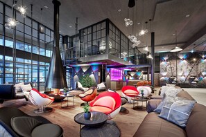A spacious lobby with modern seating, a large window, and a staircase leading to an upper level. - SCHLÖSSL-SUITE - 5* Wellness- & Sporthotel Jagdhof (Röhrnbach)