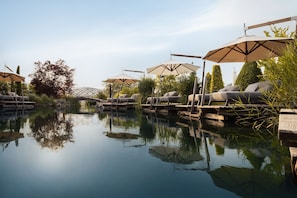 Un espace piscine extérieur paisible, doté de chaises longues et de parasols, entouré de verdure et surplombé d’un ciel dégagé.