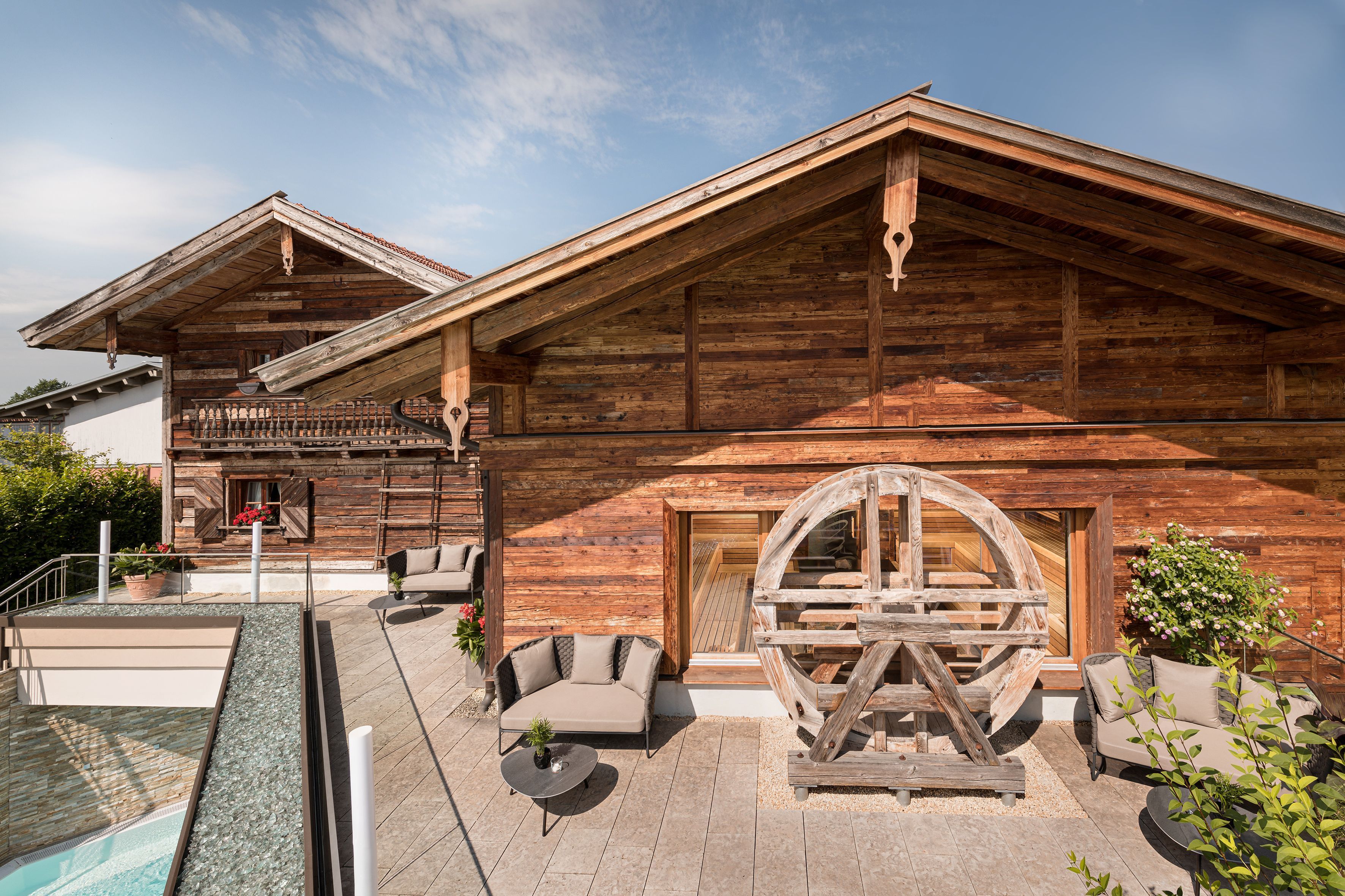 A wooden cabin with a pool, outdoor seating, and a large wooden wheel.