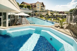 Une piscine entourée de bâtiments et de verdure, avec des chaises longues et des parasols.
