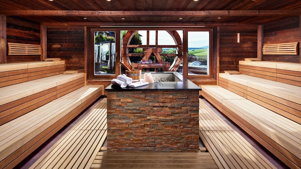 Un sauna avec des bancs en bois, un banc en pierre et une fenêtre donnant sur l’extérieur.