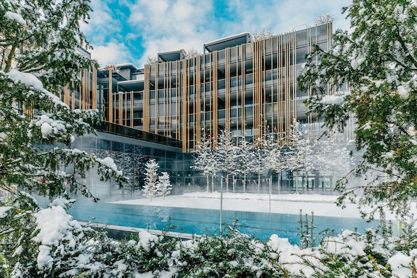 Un edificio moderno con fachada de vidrio, rodeado de árboles cubiertos de nieve y una piscina.