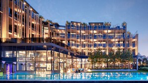 A modern hotel with a glass facade, outdoor pool, and multiple balconies.