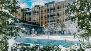 A modern building with a glass facade, surrounded by snow-covered trees and a pool.
