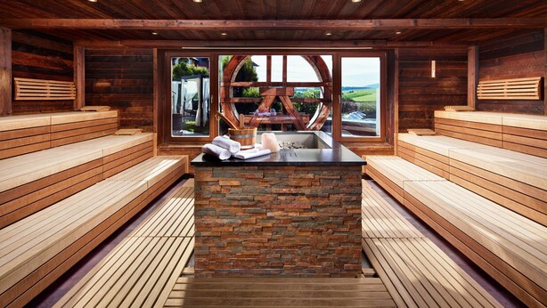 A sauna with wooden benches, a stone bench, and a window with a view of the outdoors.