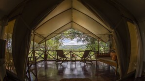 Une tente dotée d’une terrasse en bois, de deux fauteuils à bascule et offrant une vue sur un paysage verdoyant.