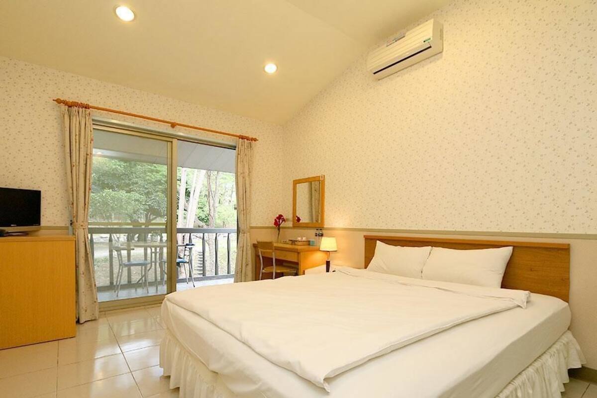 Habitación de hotel con una cama grande, un escritorio con silla, televisor y un balcón con mesa y sillas.