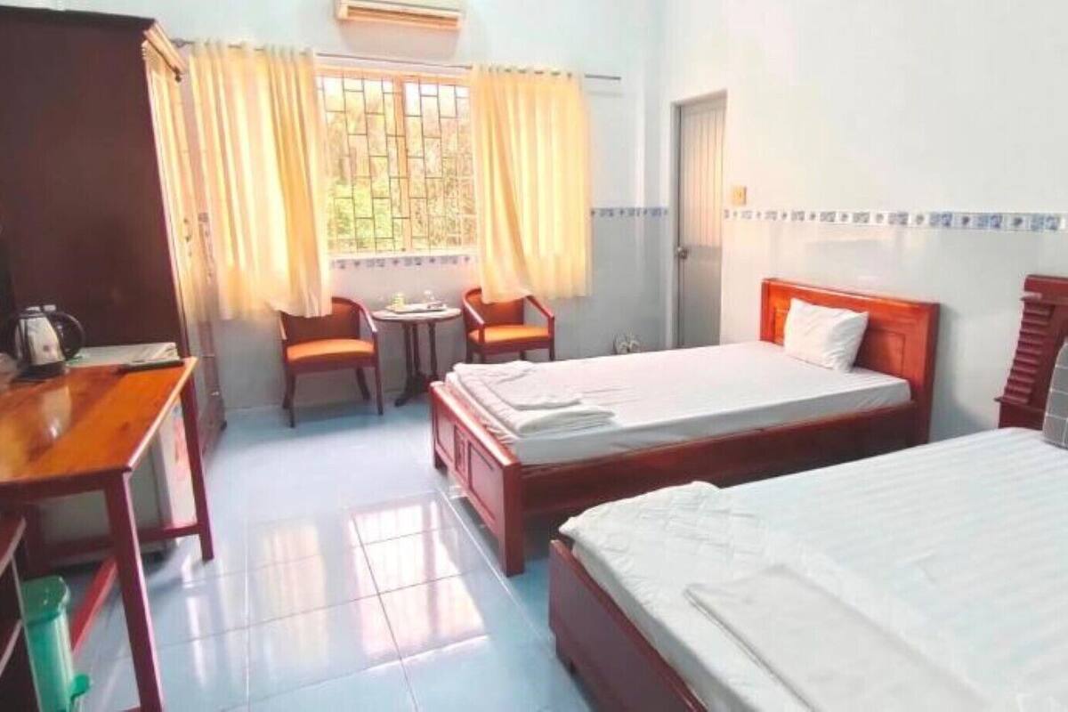 A hotel room with two beds, a desk, a chair, and a small table.