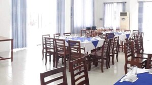 A spacious dining area with multiple tables and chairs, large windows with curtains, and a white ceiling with recessed lighting. - Ngoc Han Hotel (Thoi Son)