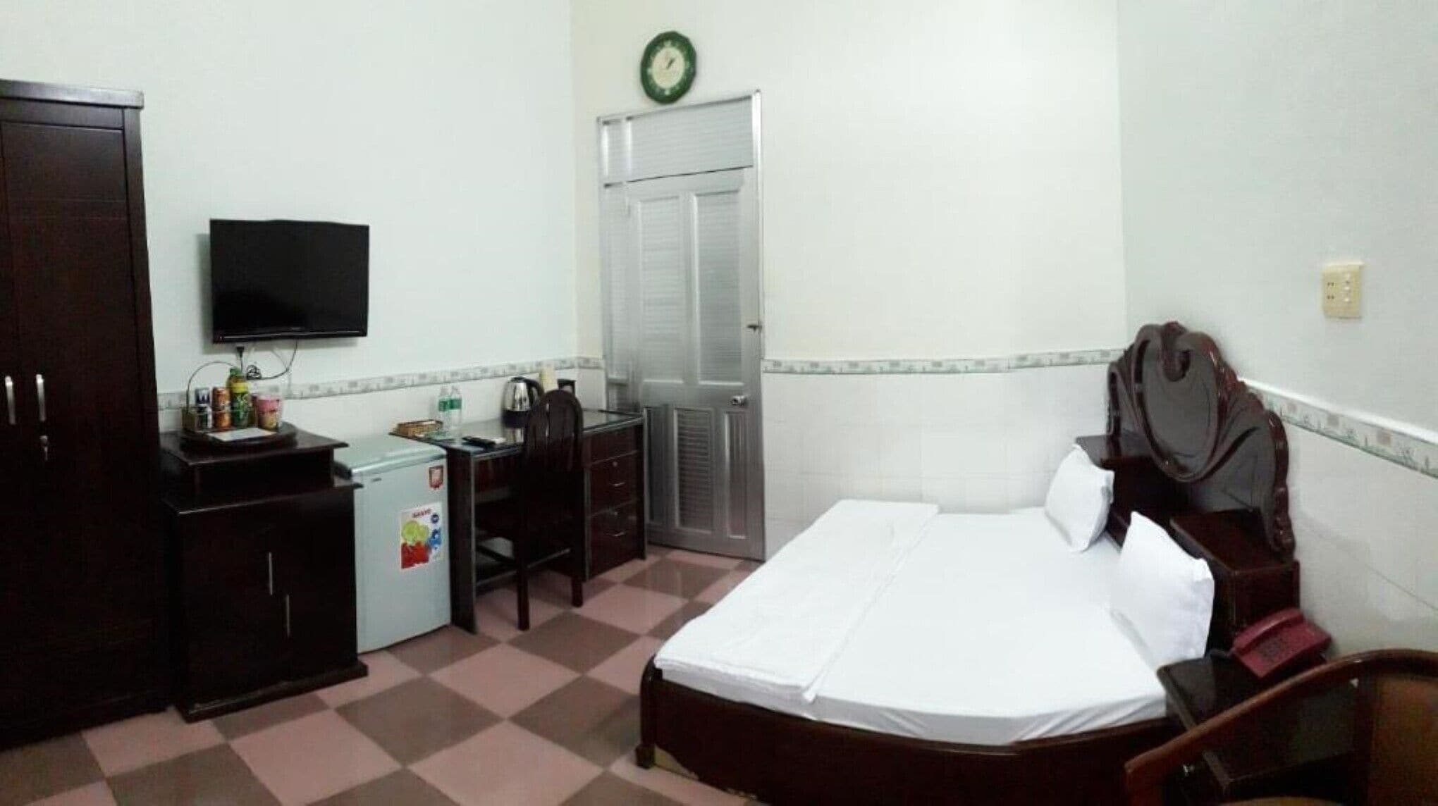 A hotel room with a bed, a desk with a computer, a chair, a wardrobe, and a television.