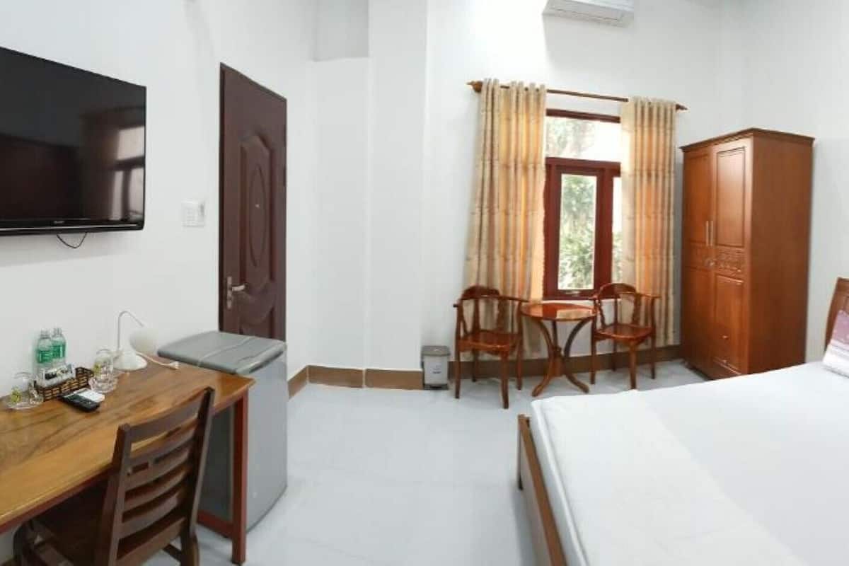 A hotel room with a bed, a desk with a chair, a TV, and a wardrobe.