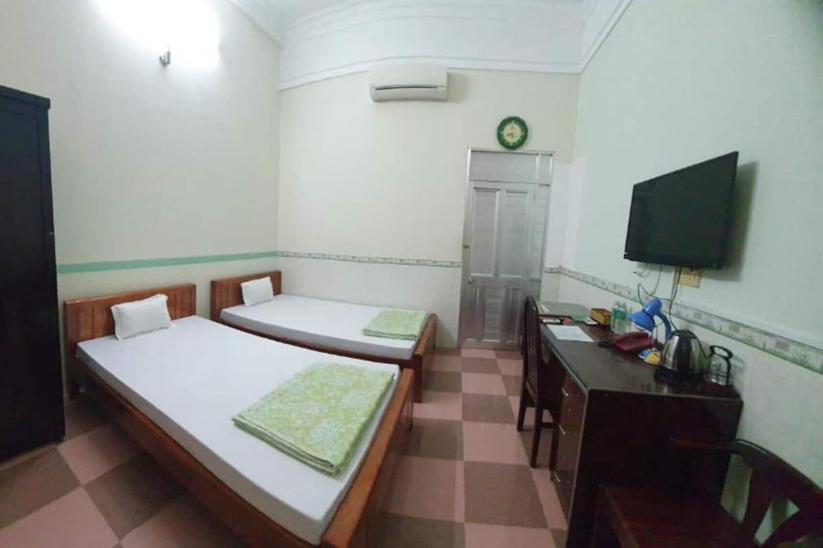 A small, clean room with two single beds, a desk with a chair, a television, and a wardrobe.