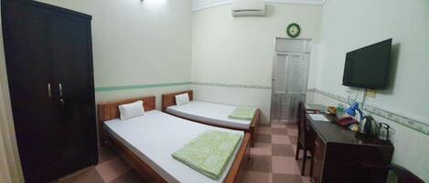 A small, clean room with two single beds, a desk with a chair, a television, and a wardrobe.